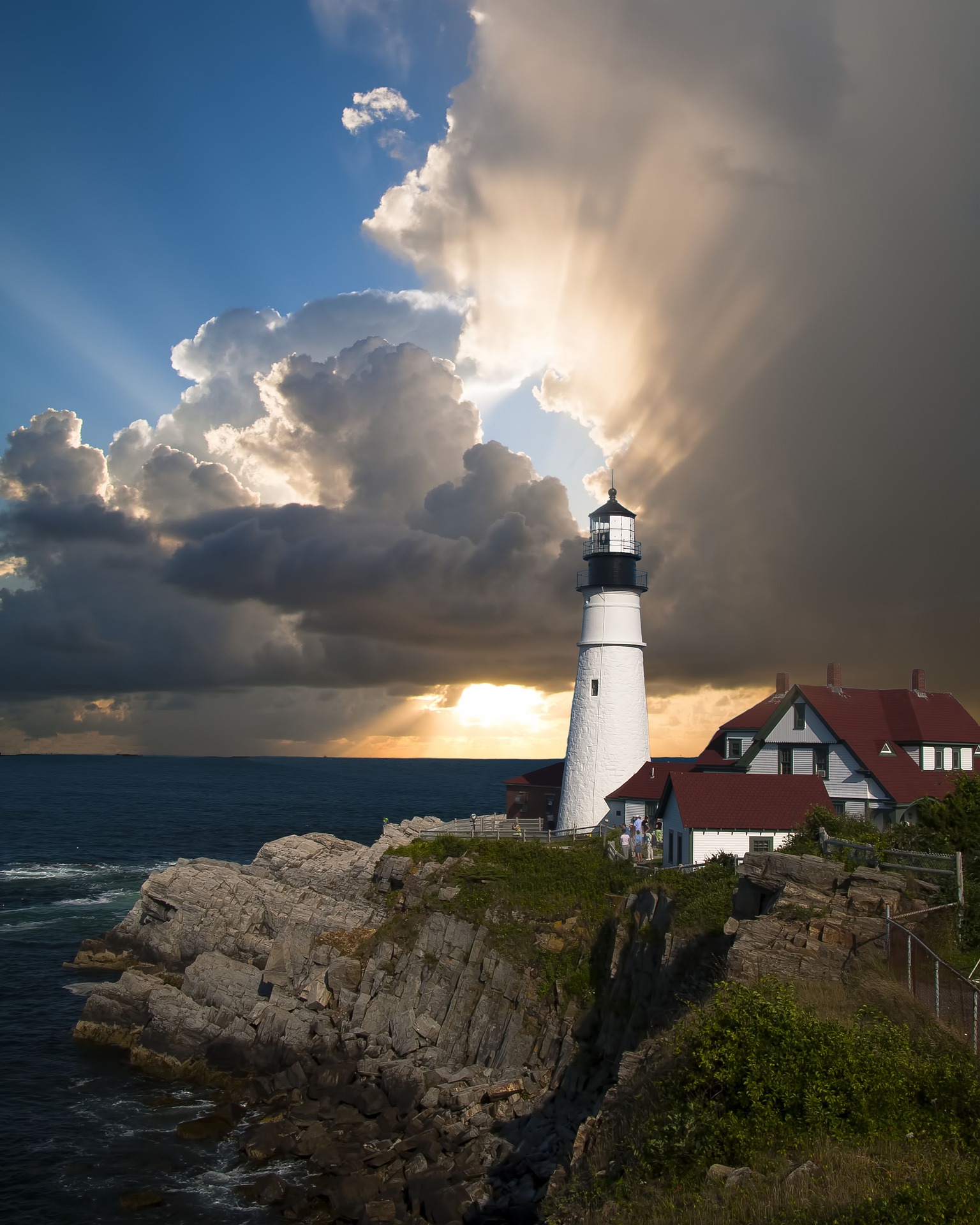 Portland Head Light lighthouse on dramatic coastal cliffs with golden sunset rays